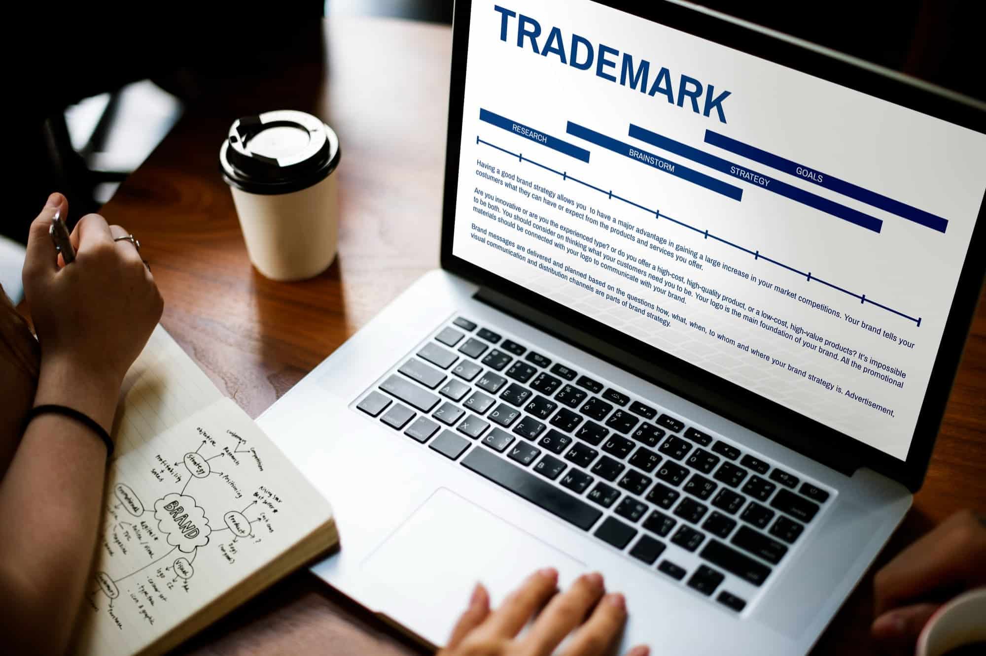 Domain A hand stamping 'PATENTED HIGH QUALITY' on a notebook with handwritten notes, placed on a wooden desk with a leather folder and a cup in the background.